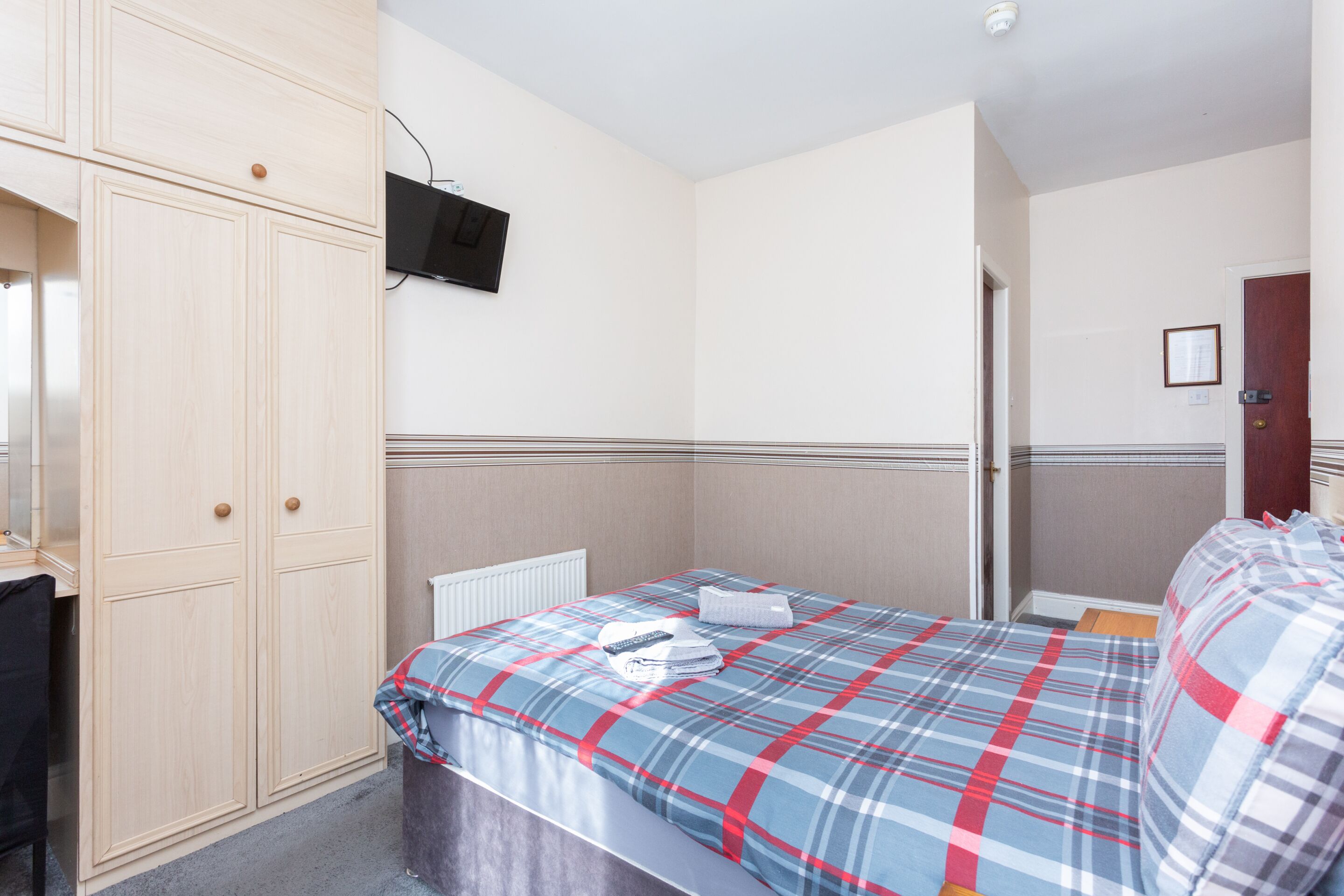 A bedroom with a bed, a wardrobe, a television mounted on the wall, and a door.