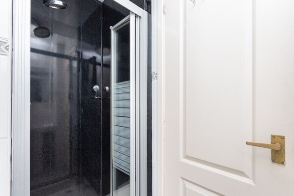 Una puerta blanca con manija de bronce, una puerta de cristal con manija metálica y una pared de baldosas negras.