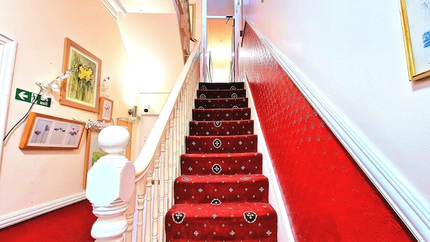 Uma escadaria com degraus carpetados em vermelho e balaústres brancos, que leva a um andar superior.