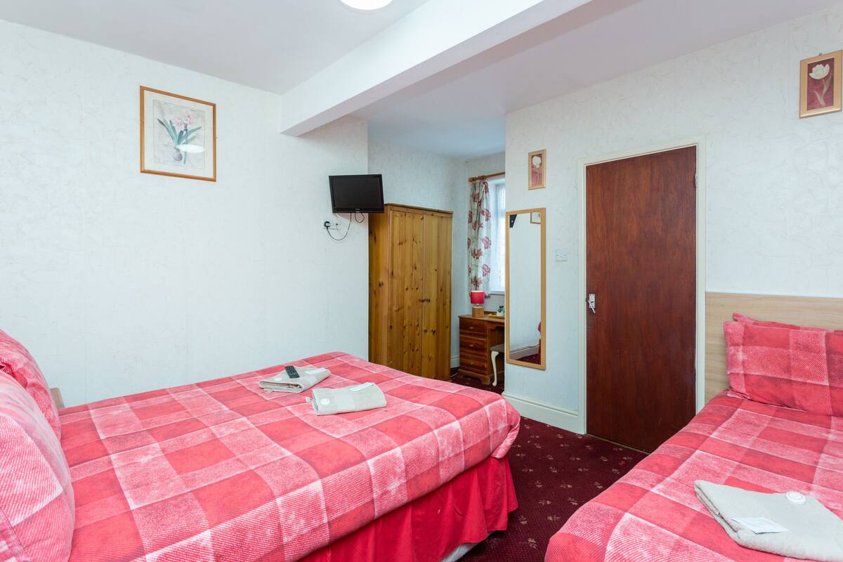 Habitación de hotel con dos camas, un armario de madera, un televisor montado en la pared y un espejo en la puerta.