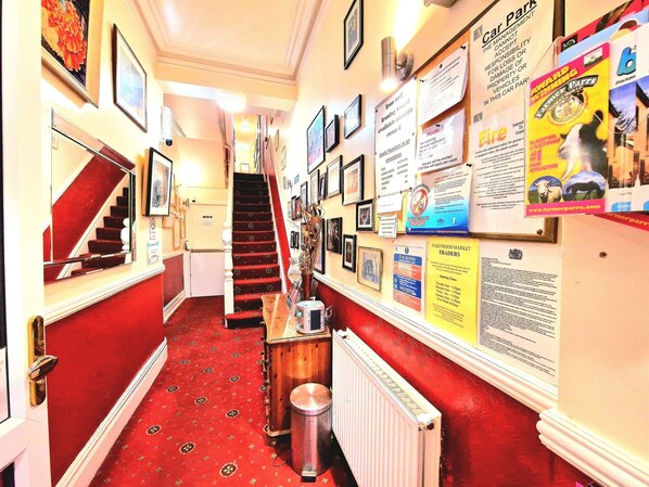 A narrow hallway with a red carpet, a staircase, and various informational posters on the walls.