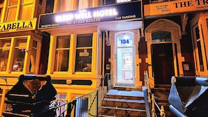 Entrada de um hotel com uma placa indicando 'The Trident Hotel' e 'Sleep Well Hotel'.