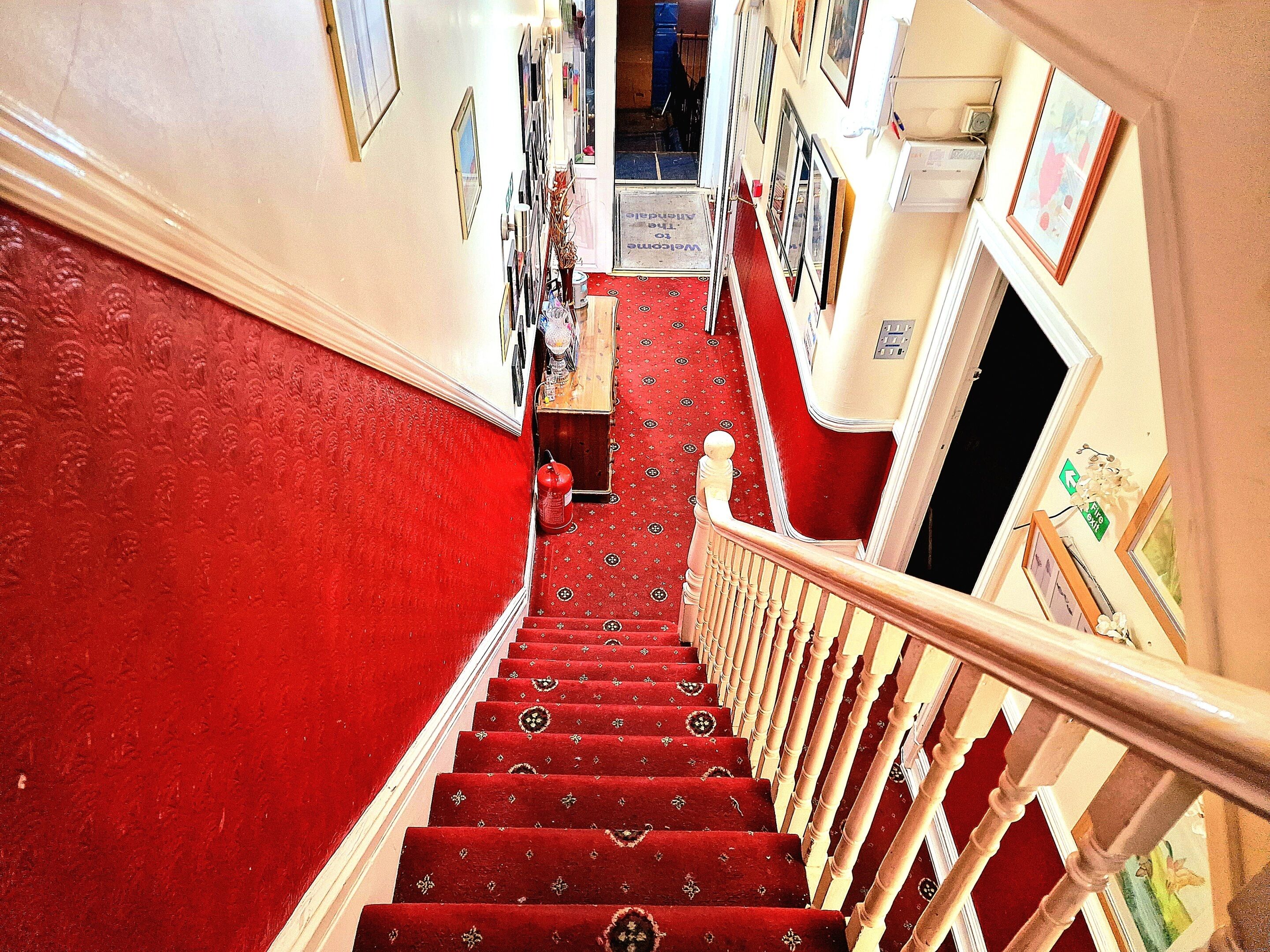 A staircase with red carpeted steps and white balusters, leading to a landing with framed pictures and a small table.