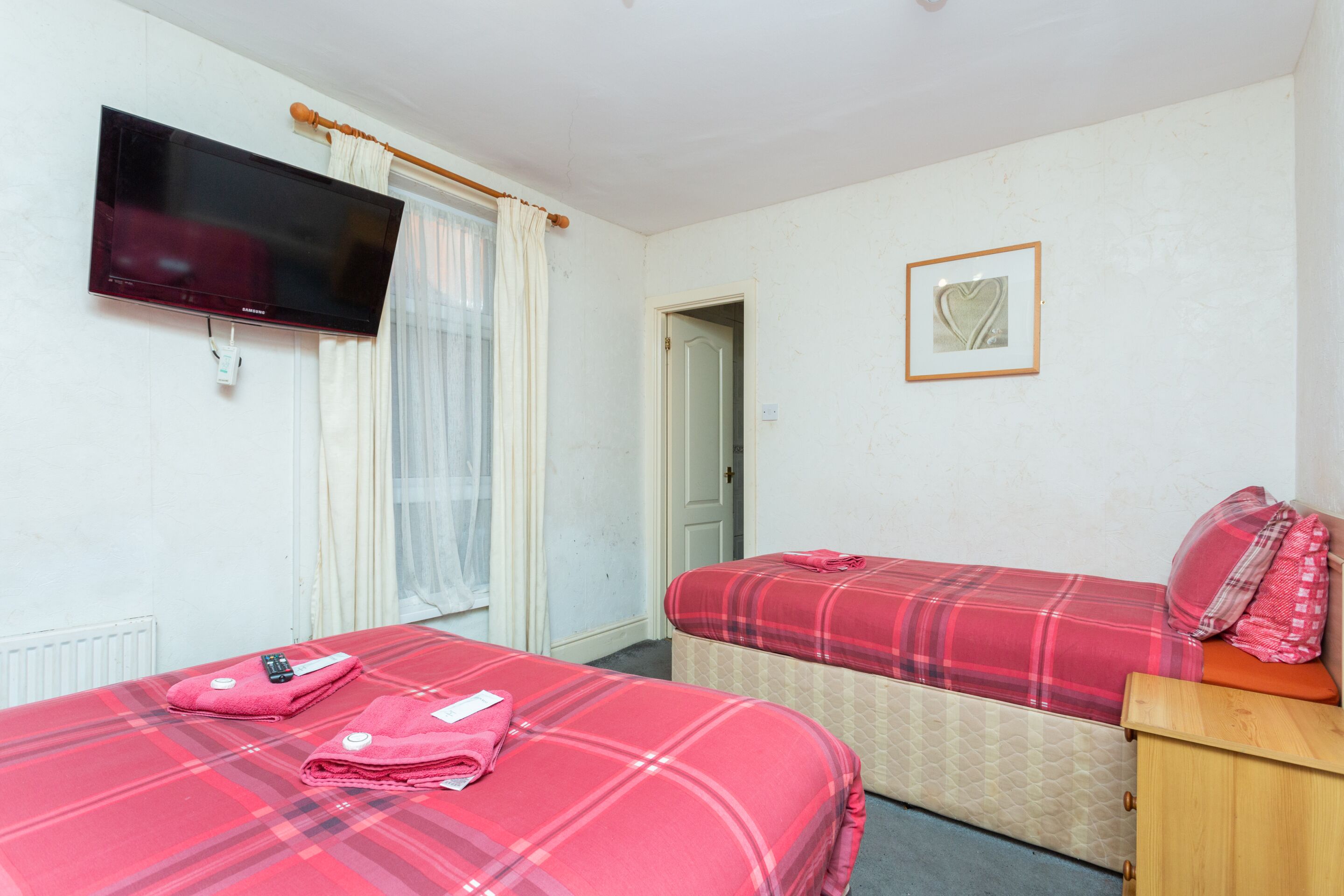 Habitación de hotel con dos camas, televisión, puerta y un cuadro enmarcado en la pared.