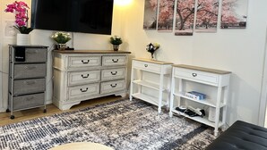 Een woonkamer met een flatscreen televisie, een witte dressoir, een klein wit tafeltje en een zwart poef.