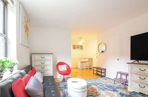 Een moderne woonkamer met een bank, een rode stoel, een witte dressoir en een televisie.