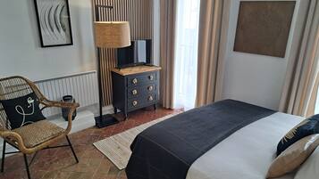 Una camera da letto ordinata con un letto, una sedia, una cassettiera, una lampada e un quadro appeso al muro.