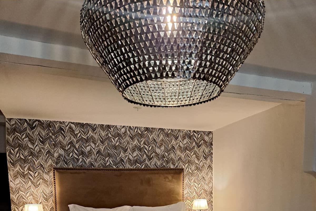 Un dormitorio con una cama grande, dos mesitas de noche con lámparas, un papel tapiz estampado y una lámpara colgante.