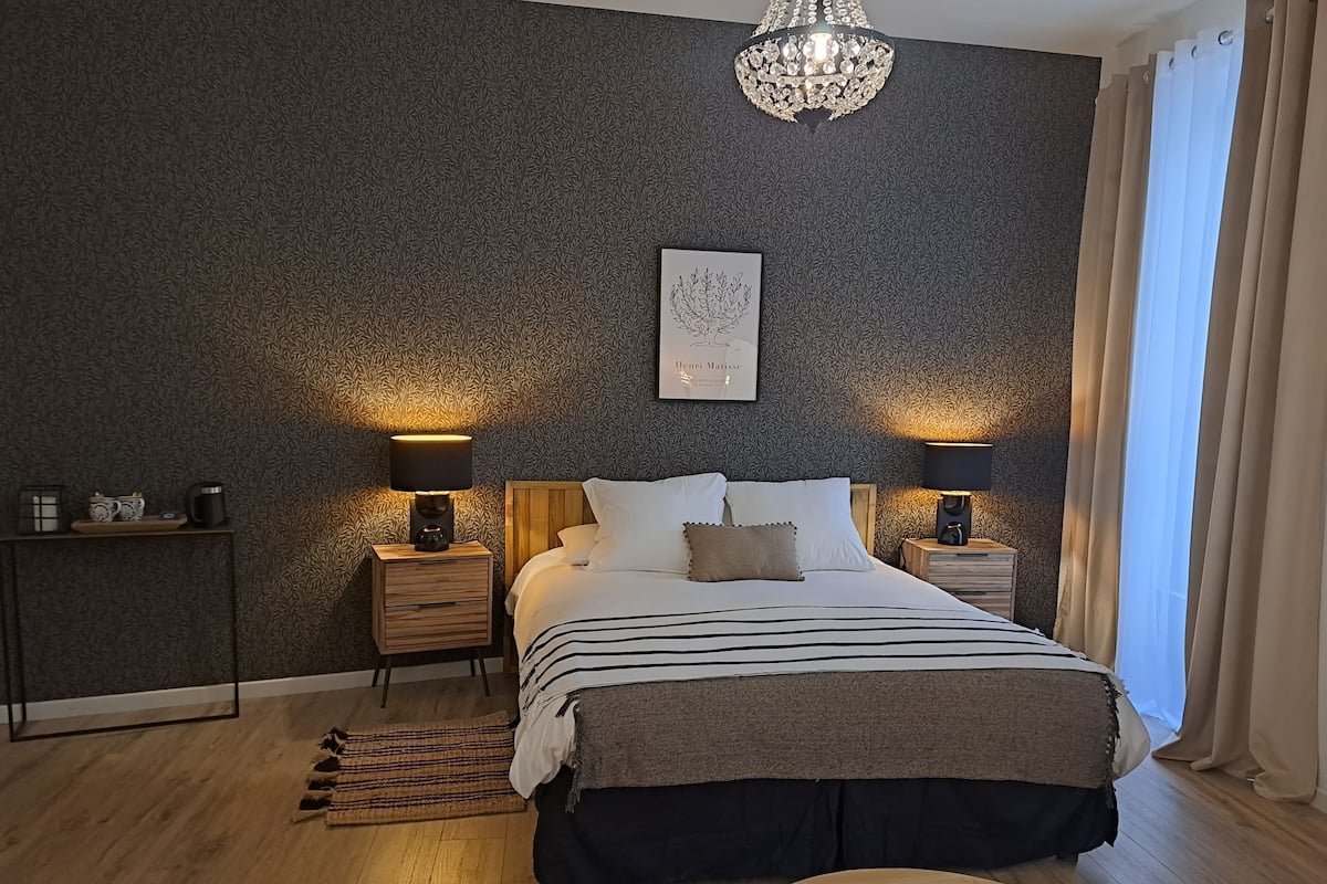 Un dormitorio moderno con una cama grande, dos mesitas de noche, una araña y una obra de arte enmarcada en la pared.