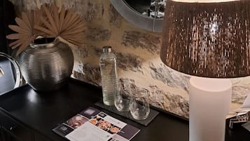 A modern interior with a round mirror, a textured lamp, a vase, and a menu on a dark countertop against a stone wall.