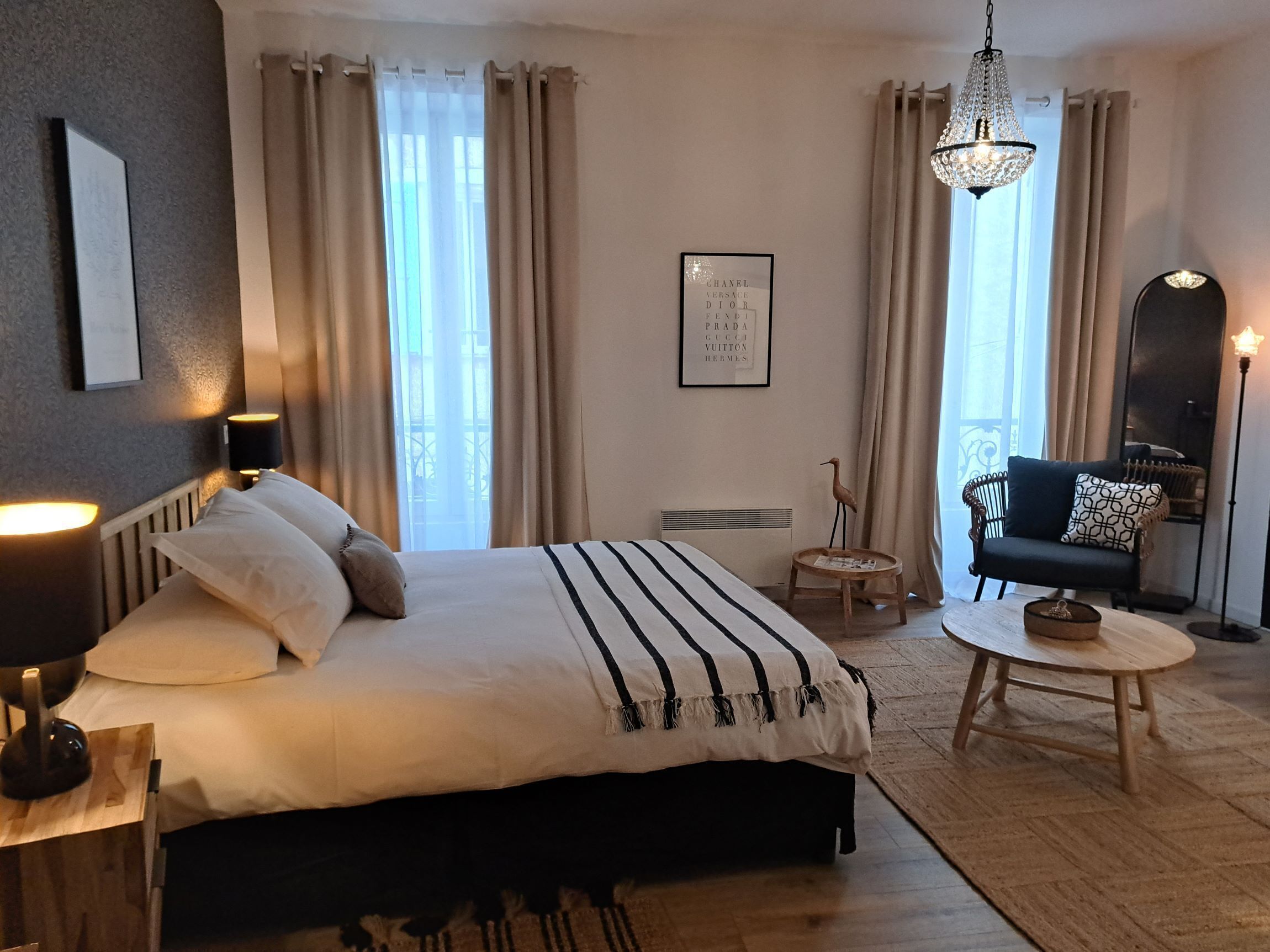 Une chambre d’hôtel avec un grand lit, une table ronde en bois, un canapé noir, un lampadaire et un lustre.