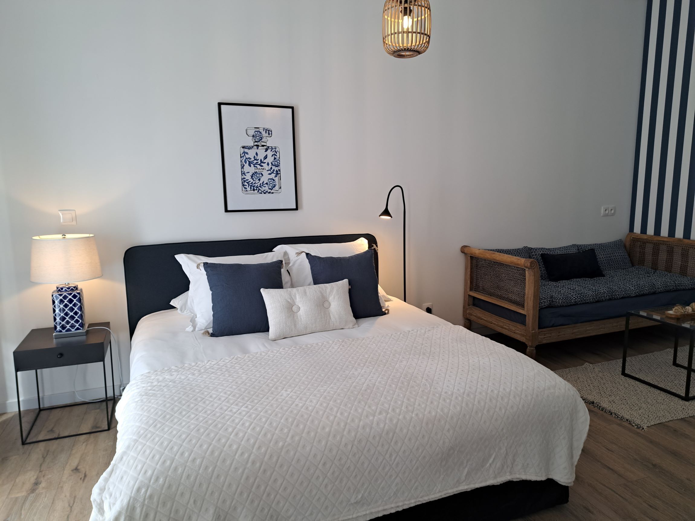 A neatly arranged bedroom with a bed, bedside table, lamp, and a hanging light fixture.