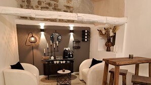 Una habitación acogedora con una mesa de madera, dos sillones blancos, una mesita redonda y una cafetera.