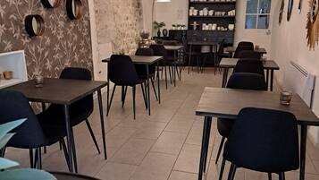 A dining area with round tables, black chairs, and a chandelier. There are wall-mounted mirrors and a shelf with teapots.
