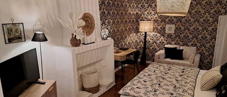 A bedroom with a bed, a desk, a chair, a TV, and a lamp.