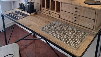 A wooden desk with drawers, a framed picture, a vase with white flowers, a black lamp, and a small table with a lamp.