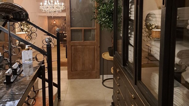 Un pasillo con puerta de madera, un candelabro, un armario con toallas y una pequeña mesa con una planta.