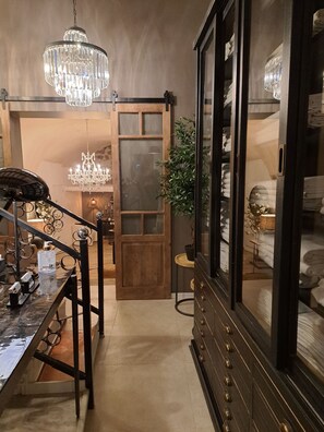 Un pasillo con puerta de madera, un candelabro, un armario con toallas y una pequeña mesa con una planta.