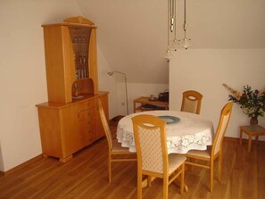 A dining area with a wooden cabinet, a table with a white tablecloth, and four wooden chairs.