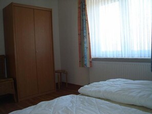 A bedroom with a wooden wardrobe, a small stool, and a bed with white bedding.