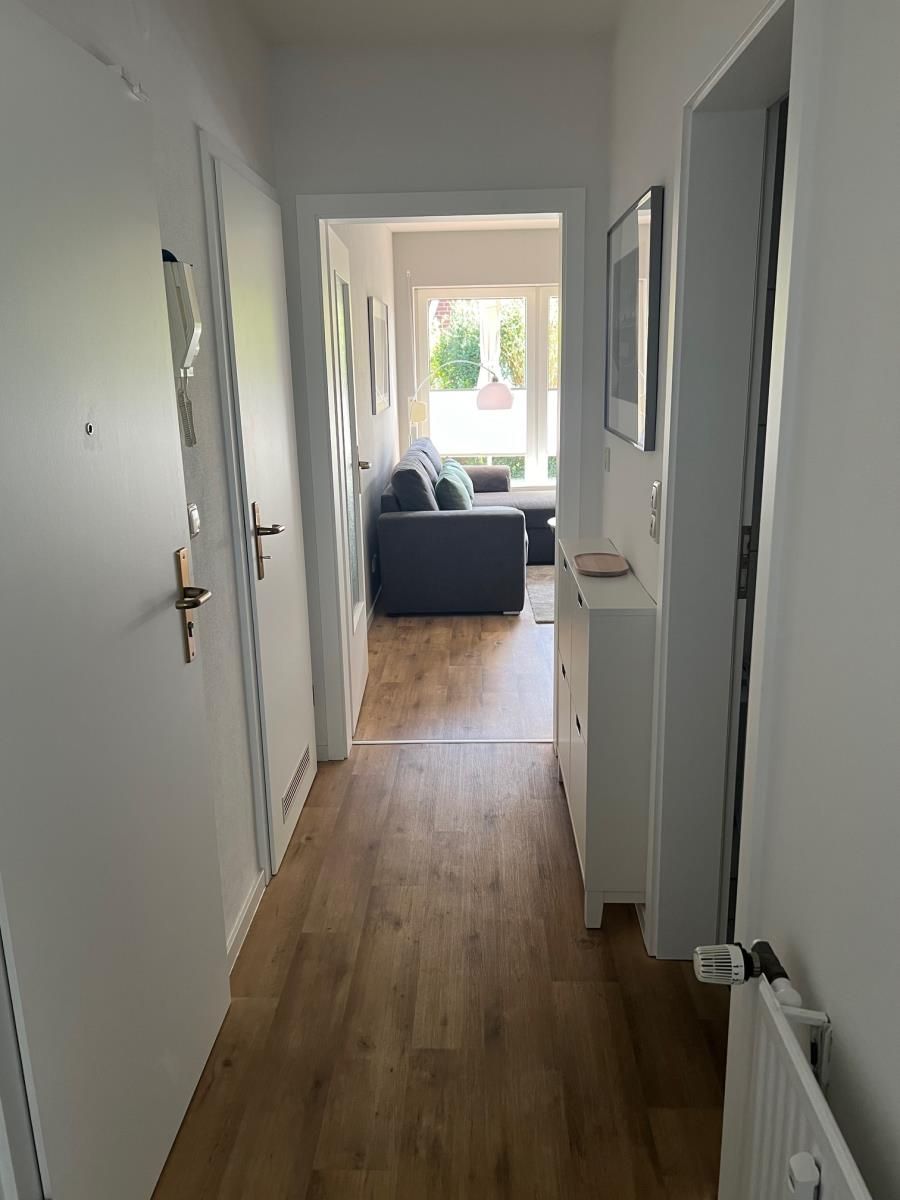 Un couloir étroit, doté d’un plancher en bois, mène à un espace de vie comprenant un canapé et une table à manger.