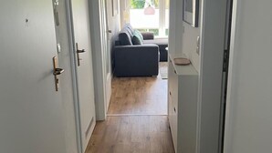 Un couloir étroit, doté d’un plancher en bois, mène à un espace de vie comprenant un canapé et une table à manger.