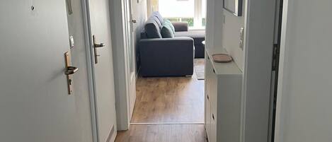 Un couloir étroit, doté d’un plancher en bois, mène à un espace de vie comprenant un canapé et une table à manger.