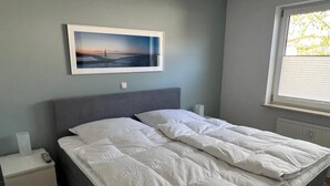 Une chambre à coucher avec un lit, une table de chevet, une commode, une fenêtre et un tableau encadré au mur.