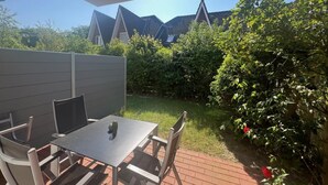 Une terrasse avec une table et des chaises, entourée d’un mur de briques et de verdure.