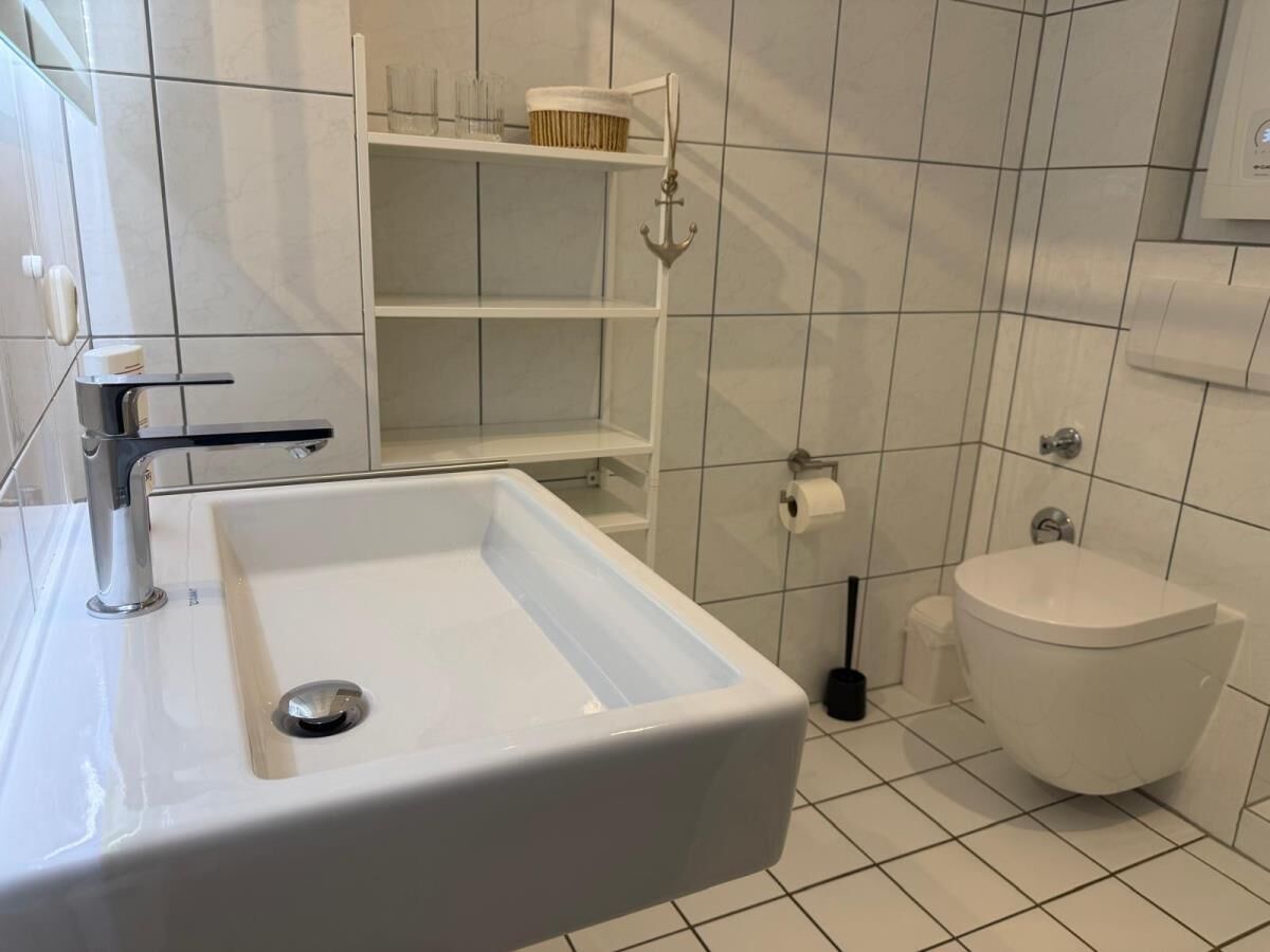 A bathroom with a white sink, toilet, and shelves with toiletries.