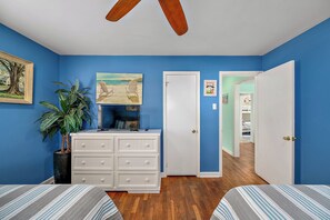 Ein Schlafzimmer mit blauen Wänden, einem Deckenventilator, einer Kommode, einem Bett und einer Topfpflanze.
