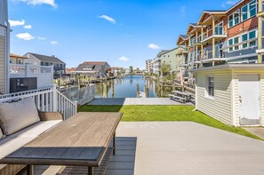 Ein Ufergrundstück mit Holzterrasse, einer Lounge und Blick auf einen Kanal mit Gebäuden am anderen Ufer.
