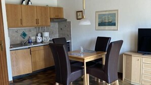 A compact living space with a dining area, kitchenette, and a television. - Häfchenweg 12 a, vacation apartment 3 (Cuxhaven)