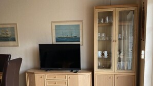 A living room with a television on a wooden cabinet, a glass cabinet with dishes, and two framed pictures on the wall. - Häfchenweg 12 a, vacation apartment 3 (Cuxhaven)