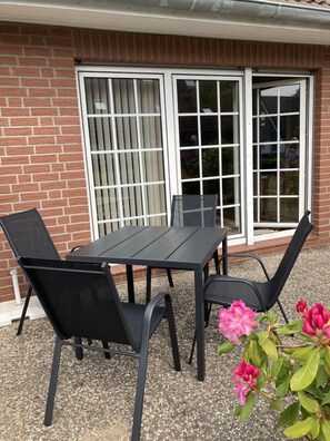 A patio with a table and chairs, a brick wall, and a sliding glass door. - Häfchenweg 12 a, vacation apartment 3 (Cuxhaven)