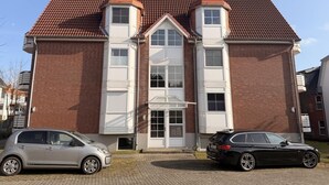 Un edificio su due piani con un tetto in tegole rosse, un ingresso centrale con una porta bianca e due auto parcheggiate davanti.