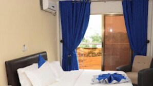 Ein Hotelzimmer mit Bett, Sessel, Schreibtisch und Fenster mit blauen Vorhängen.