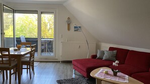Ein Wohnzimmer mit einem roten Sofa, einem Holzespeisetisch mit Stühlen, einem kleinen Tisch mit einer Pflanze und einer Heizung.