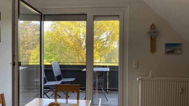 Ein Essbereich mit Tisch, Stühlen und Blick durch eine Schiebetür auf eine Terrasse im Freien mit weiteren Stühlen und einem Tisch.