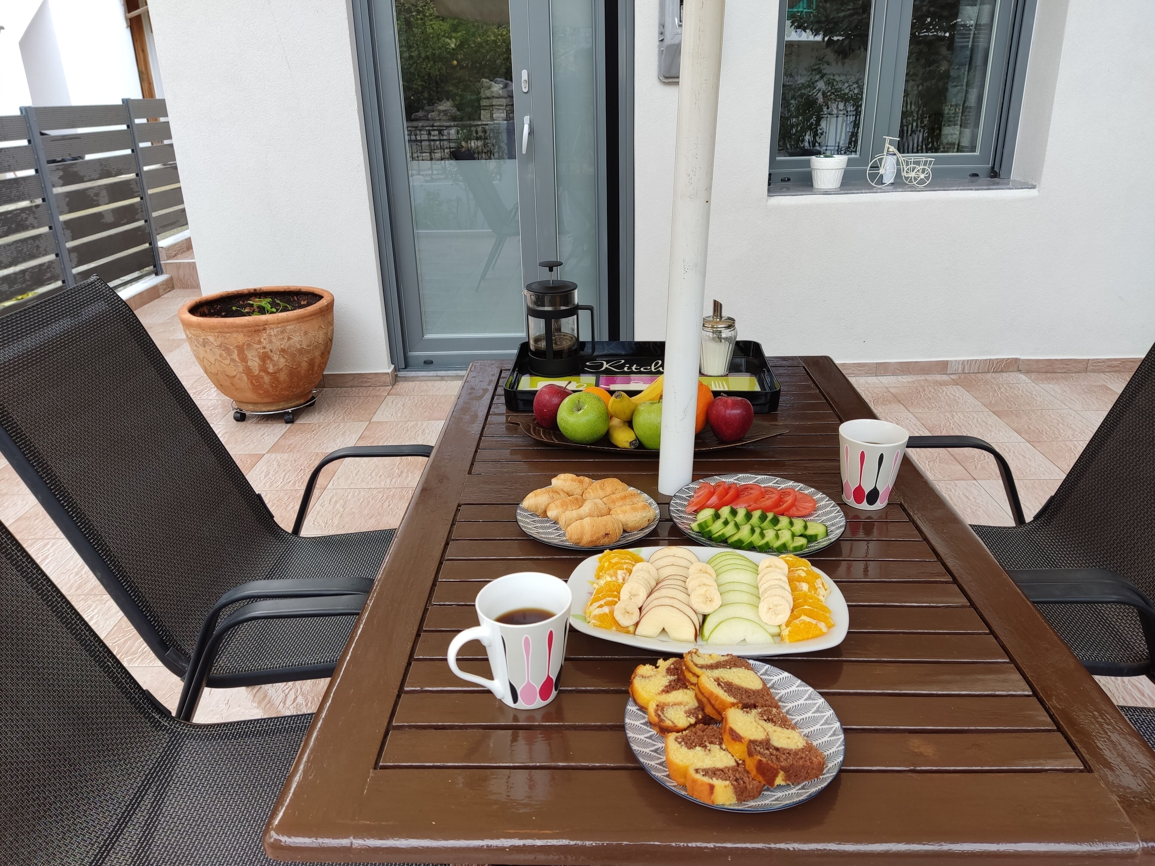 Une table dressée avec de la nourriture et des boissons, une plante en pot et une fenêtre donnant sur des arbres et des bâtiments.