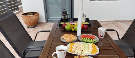 Une table dressée avec de la nourriture et des boissons, une plante en pot et une fenêtre donnant sur des arbres et des bâtiments.