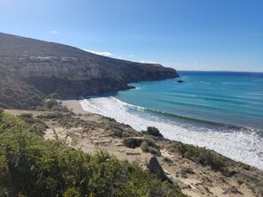 Un paysage côtier avec une plage, des falaises rocheuses et un ciel bleu dégagé.