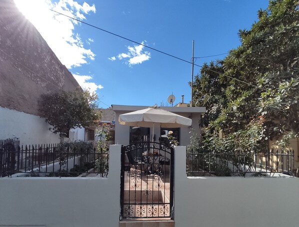 Une entrée fermée par un portail, un petit espace patio, un mur blanc et une montagne en arrière-plan.