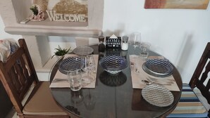 A round glass table set with patterned bowls, glasses, and cutlery, surrounded by wooden chairs with cushioned seats. - Irini's Home Pitsidia 
Family friendly (Πιτσίδια)