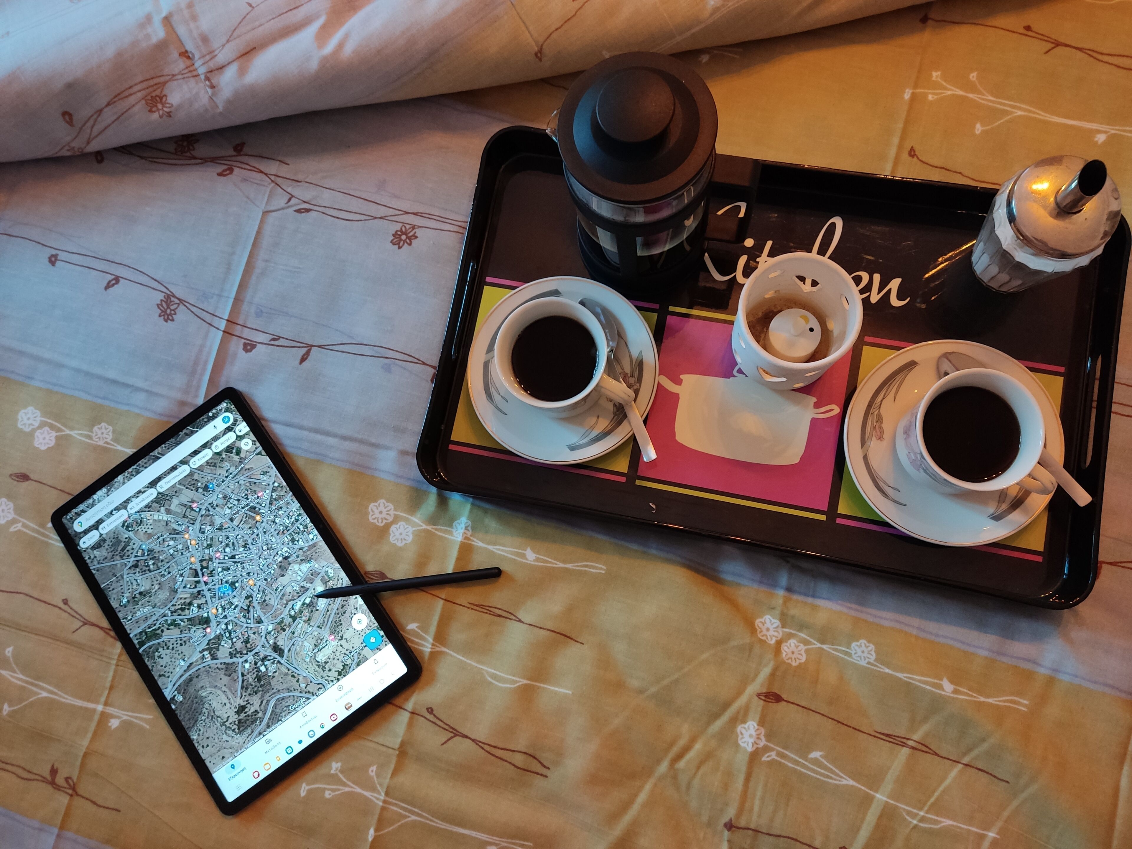 A tray with three cups of coffee, a teapot, and a smartphone displaying a map.