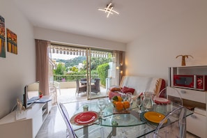 A modern living room with a glass dining table, a sofa, and a TV. - Appartement Menton Garavan Avec Superbe Piscine vue mer Proche Italie & Monaco (Menton)