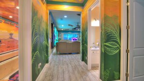 A hallway with a mural, a bed, and a bathroom with a green leaf design. - 2 Side-by-side homes w Bowling, 1GB wifi, videowall TVs, ensuites, sleep 80 (Kissimmee)