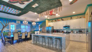 A modern kitchen with white cabinets, a large island with bar stools, and a mural of a tree and sky. - 2 Side-by-side homes w Bowling, 1GB wifi, videowall TVs, ensuites, sleep 80 (Kissimmee)
