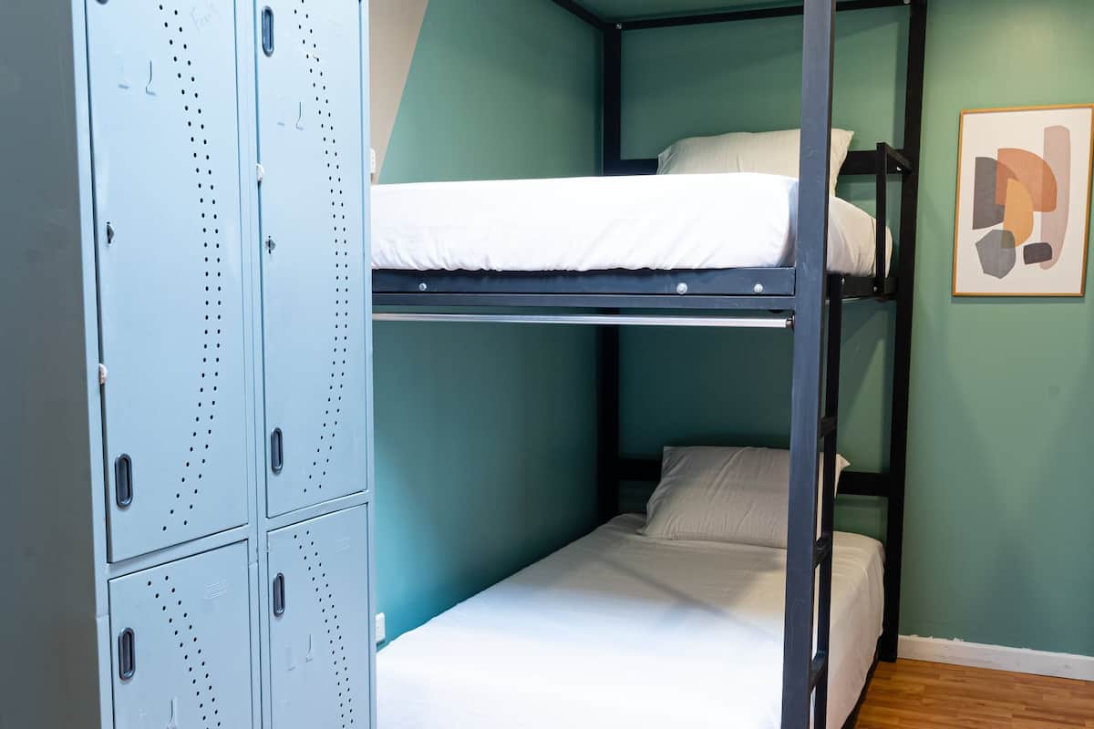A bunk bed room with a metal wardrobe and a framed picture on the wall.