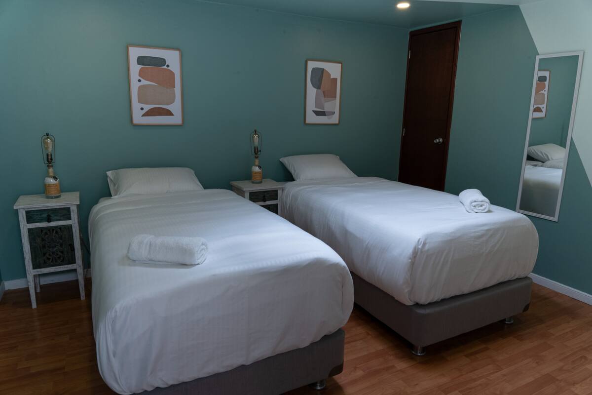 A room with two beds, wooden flooring, teal walls, and framed artwork.